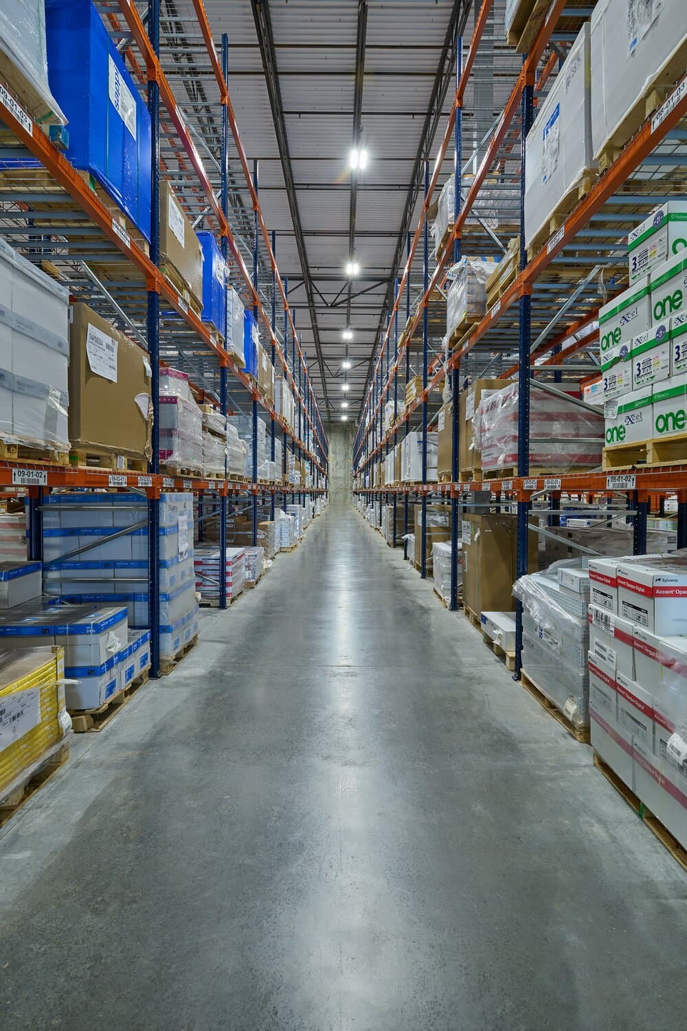 Interior image of warehouse with poured concrete floors, shelving and overhead lighting.