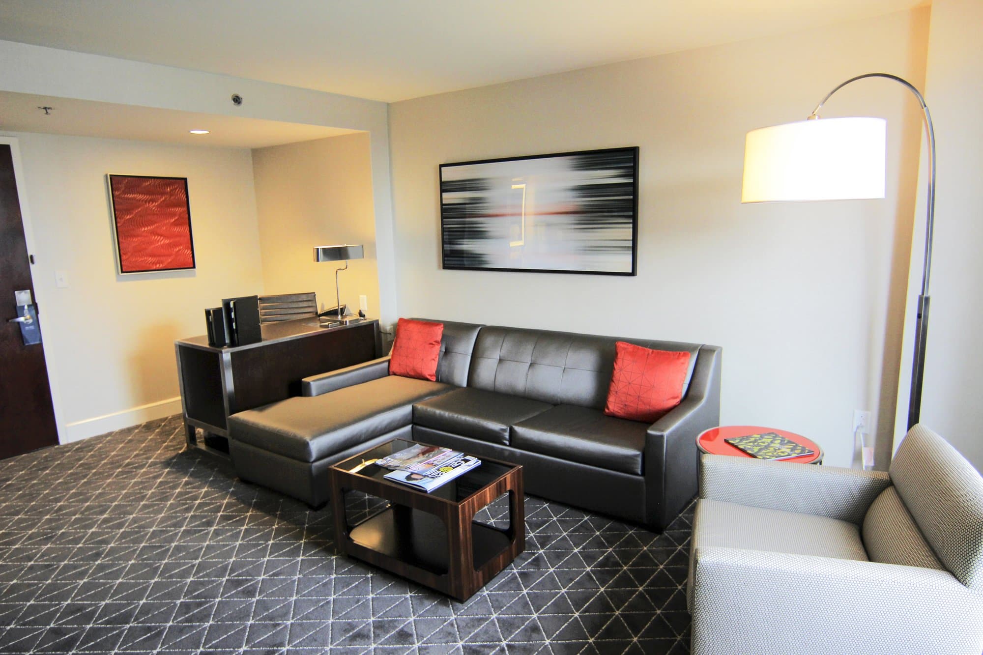 Hotel room living space with a black leather couch and a dark geometric carpet design.