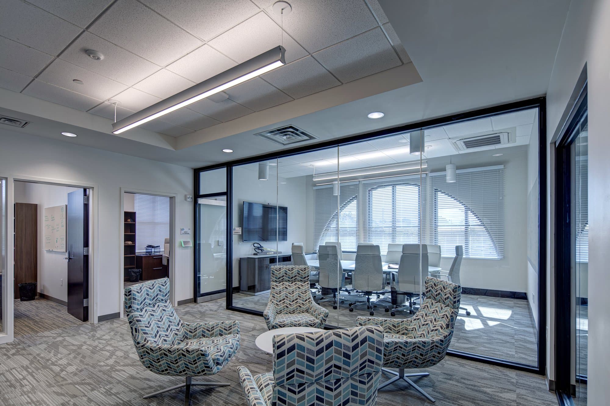 Glass walled meeting room with additional seating outside and offices.