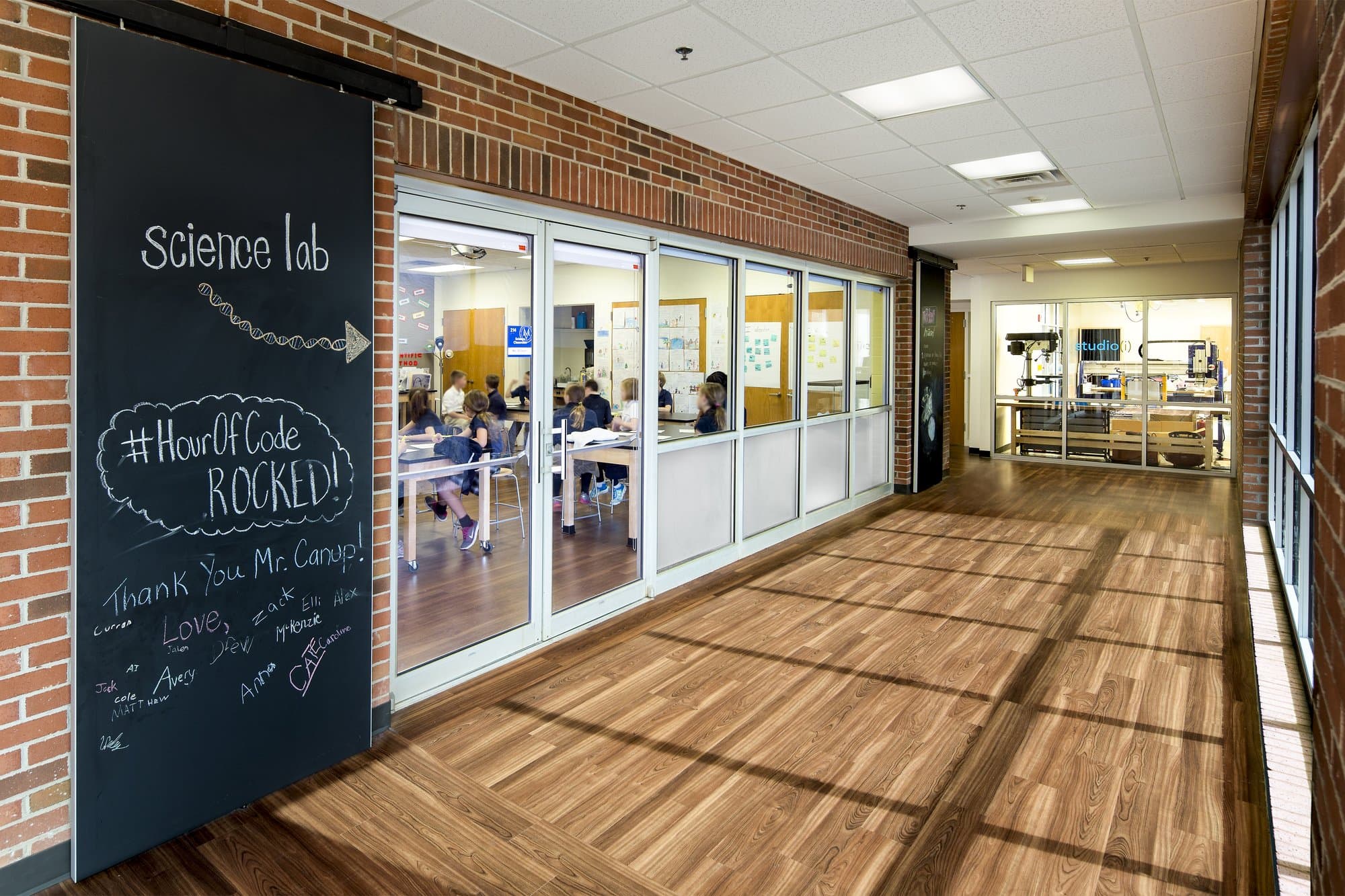 A floor-to-ceiling chalkboard directs students to the "science lab" in a brick hallway with wooden floors.