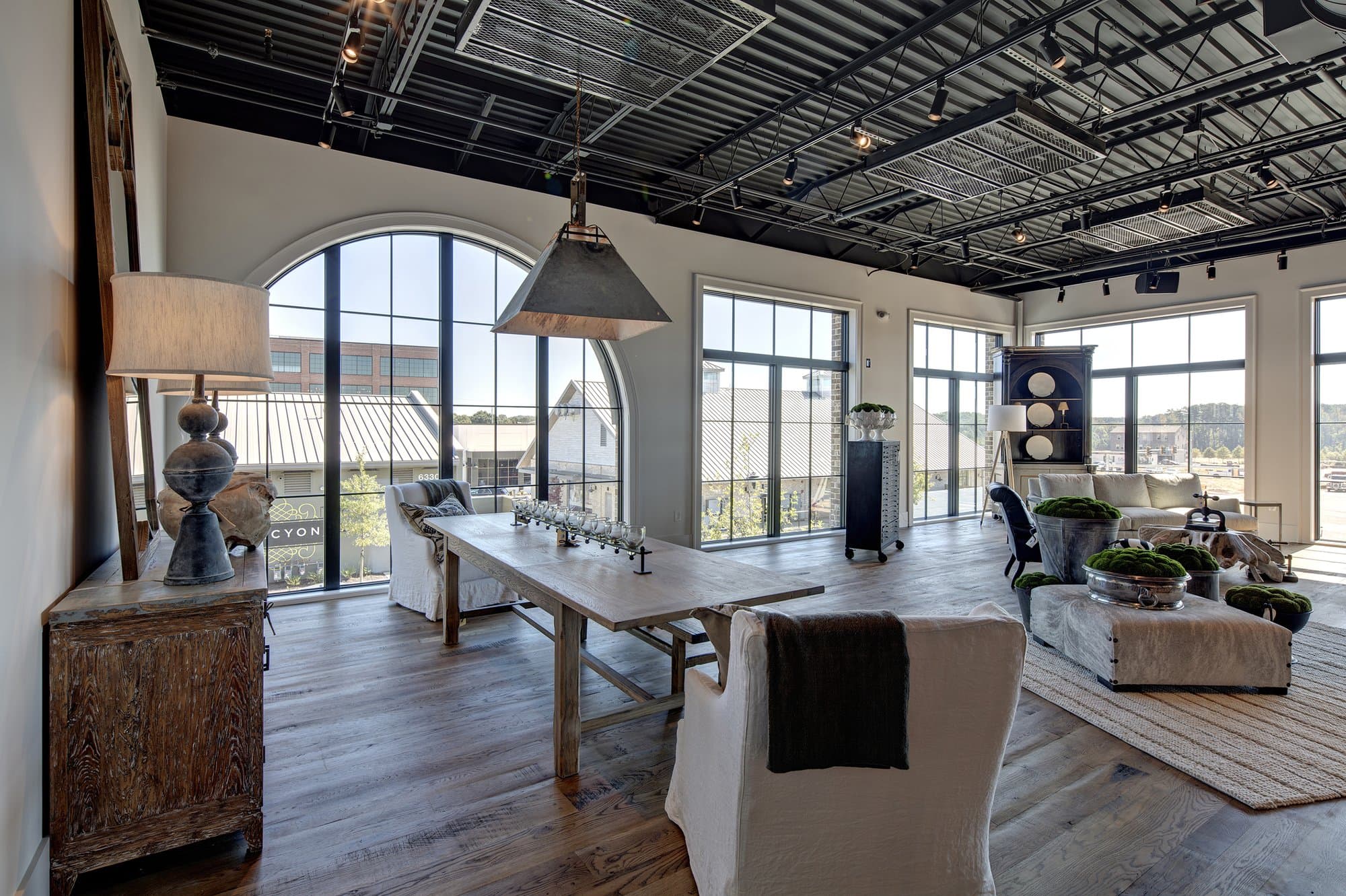 Furniture showroom with an exposed metal ceiling and dark wooden floors. Large windows illuminate the room.