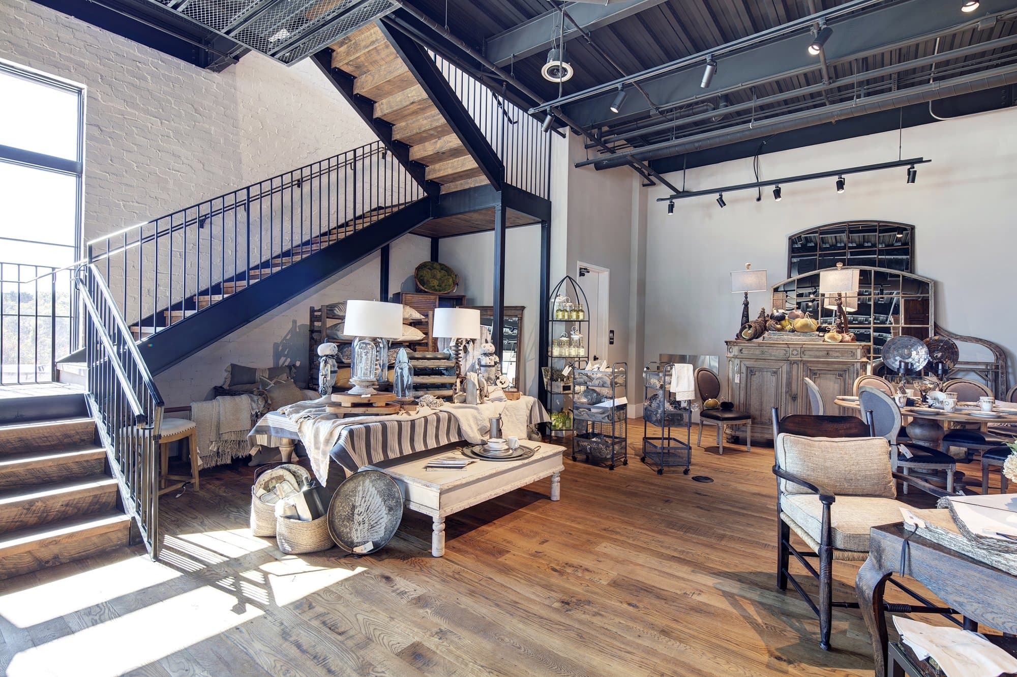 A furniture showroom with a grand staircase and wooden floor.