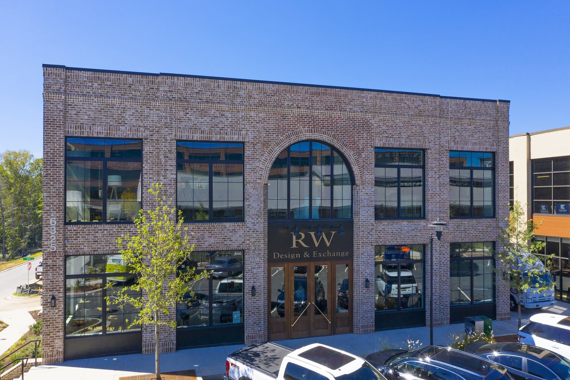 A building exterior with a light brick facade and grand wooden doors set in front of a deep blue sky. 