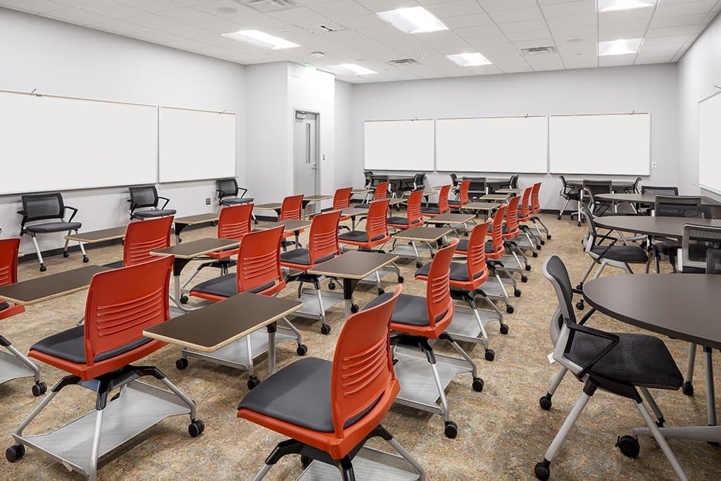 Classroom with orange seated desks and whiteboards on the wall.