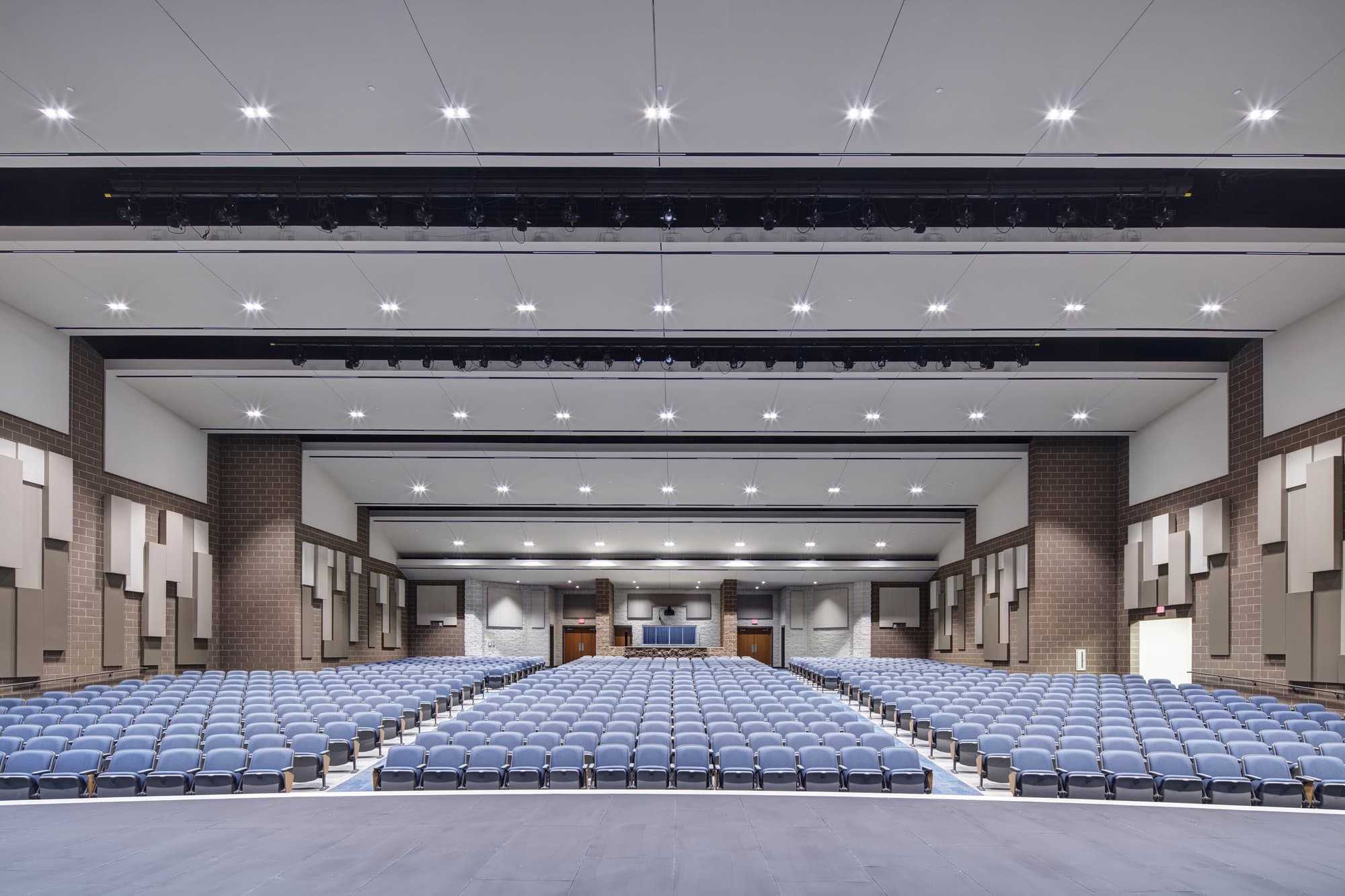 Rows of blue chairs seen from the stage of a wide open high school auditorium.