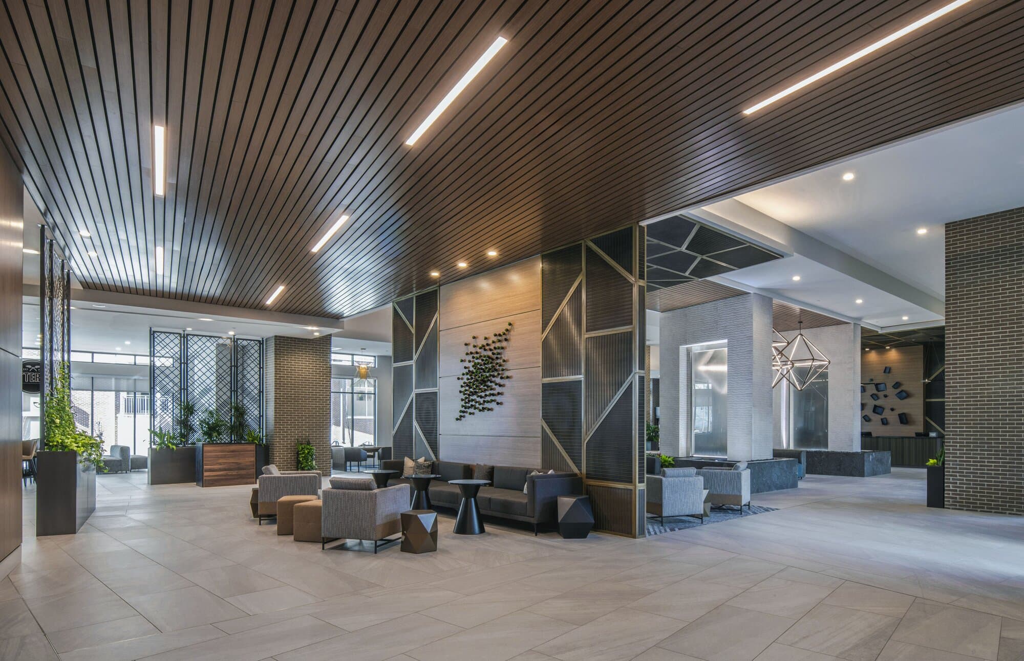Large lobby area with wood panels on the ceiling mixed with light bars and recessed lights. Multiple seating arrangements in various locations.
